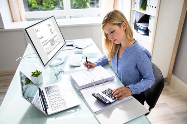 Young Businesswoman Calculating Bill With Computer And Laptop On Desk